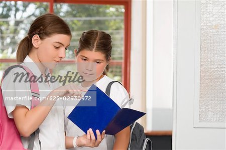 Close-up of a schoolgirl showing her textbook to another schoolgirl