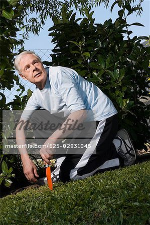 Senior man kneeling in a garden and holding a gardening fork