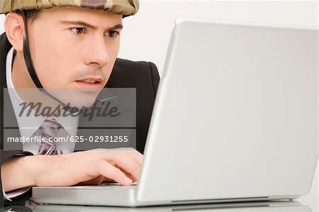 Close-up of a businessman wearing an army helmet and working on a laptop