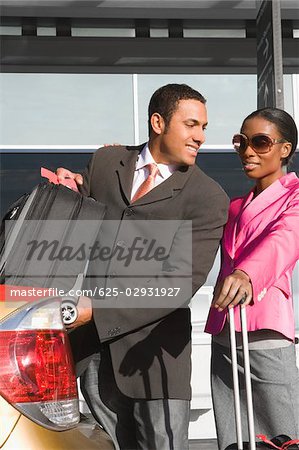 Businessman loading his suitcase on a car trunk with a businesswoman standing beside him