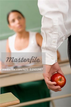 Close-up of a person's hand holding an apple in front of a female teacher