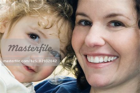 Close-up of a mid adult woman carrying her daughter and smiling