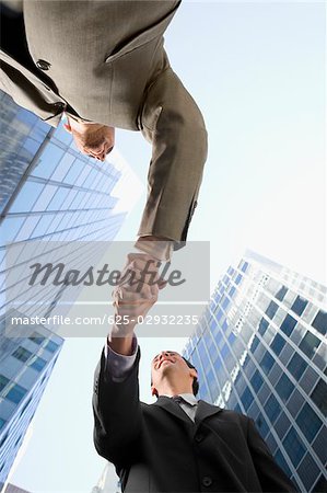 Low angle view of two businessmen shaking hands and smiling