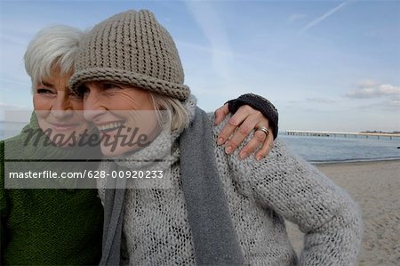 Two mature women laughing and embracing each other at Baltic Sea beach