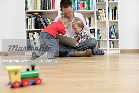 Father with two sons trying to using a mobile phone and a laptop