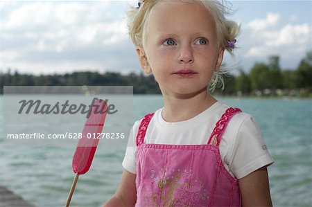 Little blond girl eating an ice lolly on a wooden footbridge