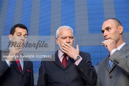 Three businessmen smoking in front of an office building