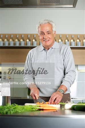 Gray-haired man is cutting vegetables in a kitchen, selective focus