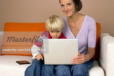 Mother and son (4-5 Years) sitting on a sofa und using a laptop