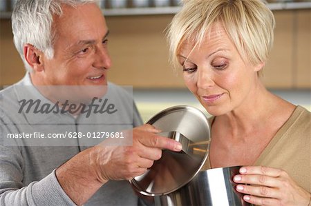 Gray-haired man letting a woman see what he has cooked, close-up