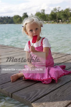 Little blond girl eating an ice lolly on a wooden footbridge
