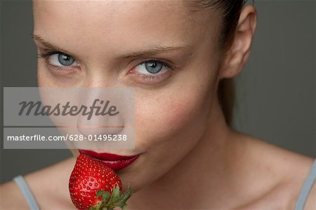 Young woman with a red strawberry under her red lips (part of), close-up