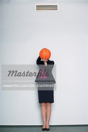 Businesswoman covering face with a basketball