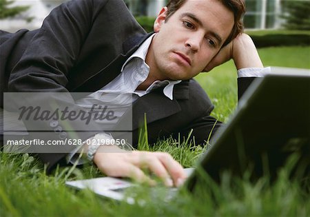 Businessman lying on grass while using a laptop