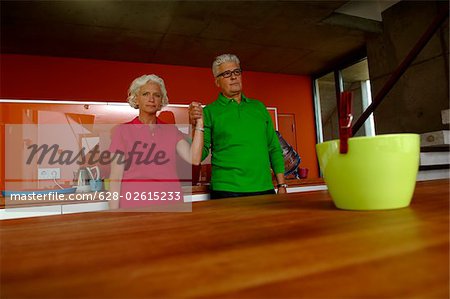 Senior couple holding hands standing in domestic kitchen
