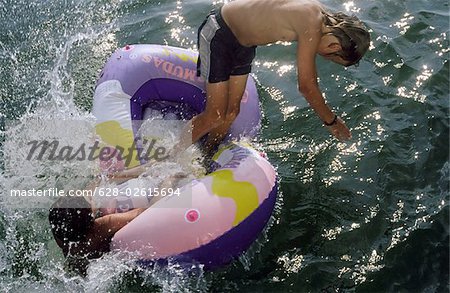 Two Boys jumping out of a Rubber Dinghy at the same Time - Fun - Youth - Lake