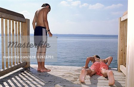 Boy lying procumbently next to his upright standing Friend - Swimming - Friendship - Leisure Time - Lake