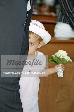 Little Girl in a white Dress with a Bunch of Flowers in her Hand hiding behind a Grown-Up - Bashfulness - Church - Celebration - Baptism - Christianity