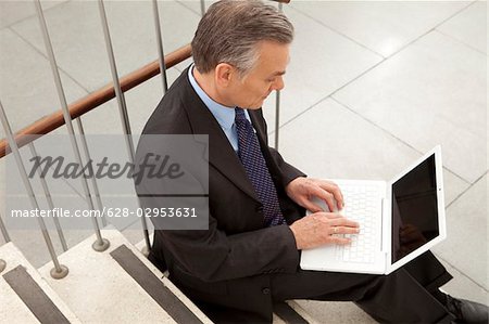 Businessman using laptop on stairs, Munich, Bavaria, Germany