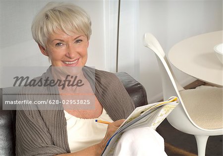 Senior woman sitting with crossword puzzle on sofa