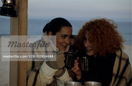 Two female friends with Cups under one Blanket - Coldness - Friendship - Beach - Season