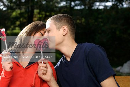 Teenage couple holding heart-shaped lollypops in their hands and kissing