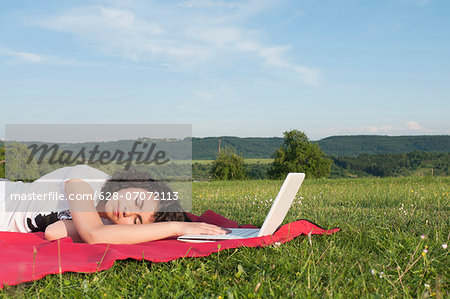 Girl with laptop sleeping in meadow