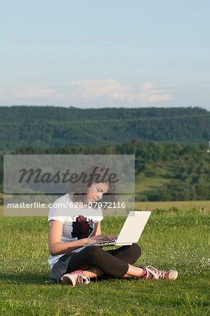 Girl using laptop in meadow