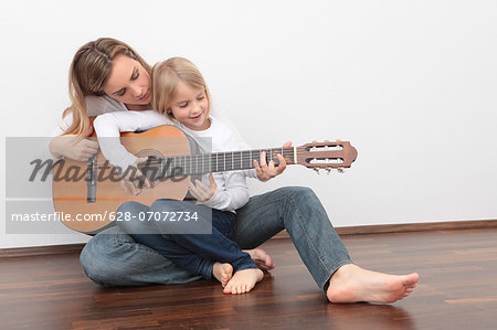 Daughter playing guitar on mother's lap