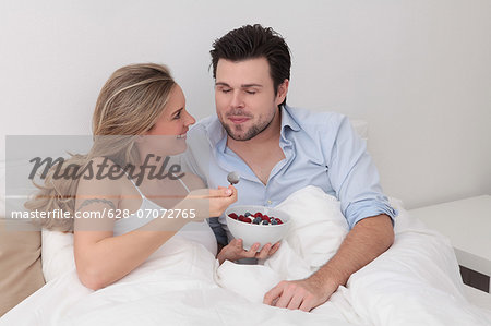 Couple eating berries from bowl in bed
