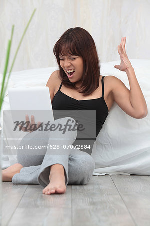 Screaming young woman using laptop in bedroom