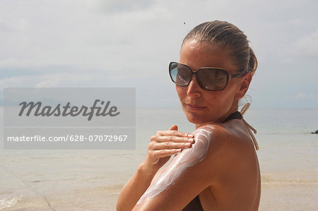 Woman on beach applying suntan lotion, Thailand