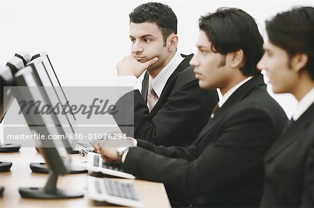 Side profile of three businessmen working on computers in an office