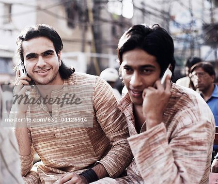 Two young men sitting in a rickshaw and talking on mobile phones