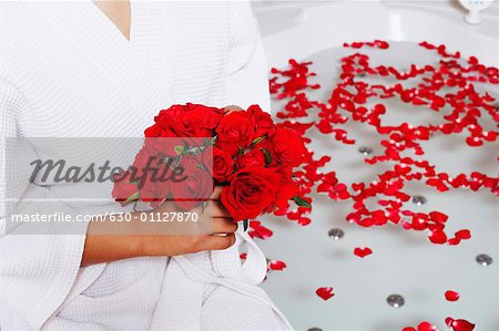 Mid section view of a woman holding a bunch of roses near a bathtub