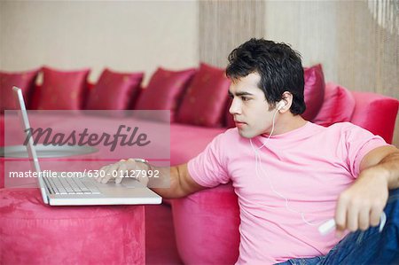 Young man listening to an MP3 player and using a laptop