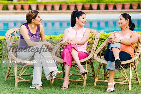 Three young women sitting on chairs at the poolside