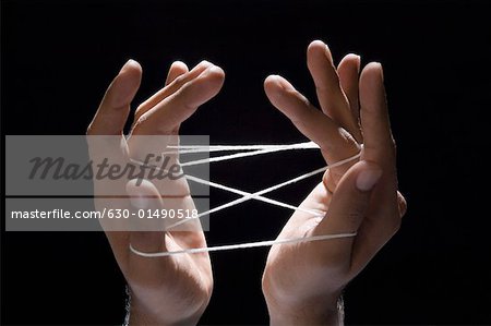 Close-up of a person's hands playing cats cradle with a rubber band
