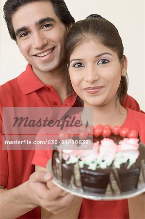 Portrait of a young couple holding a chocolate cake and smiling