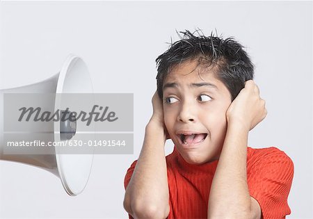 Close-up of a boy covering his ears with his hands and looking at a megaphone