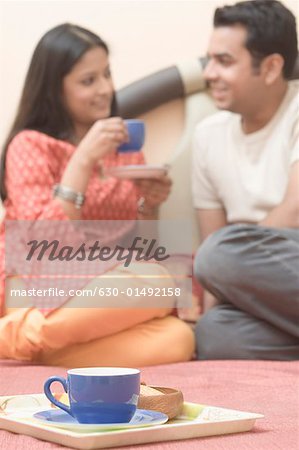 Tea cup on a tray with a young couple sitting on the bed in the background