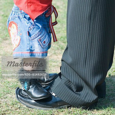 Low section view of a baby girl standing on her father's feet