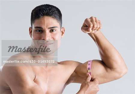 Portrait of a young man measuring his biceps with a tape measure