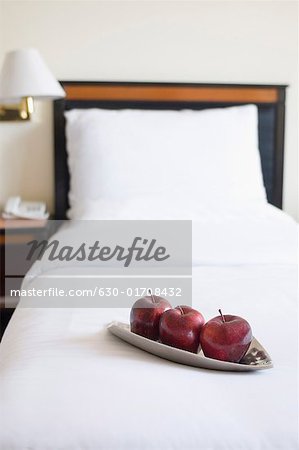 Three apples in a plate on the bed in a hotel room