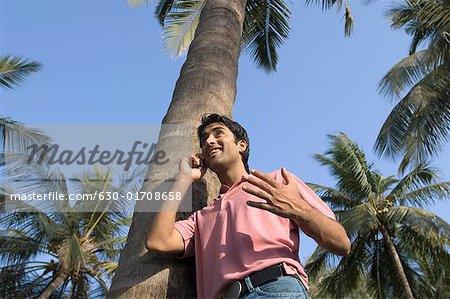 Low angle view of a young man leaning against a tree and talking on a mobile phone