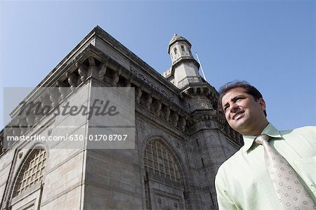 Low angle view of a businessman smiling in front of a monument, Gateway of India, Mumbai, Maharashtra, India