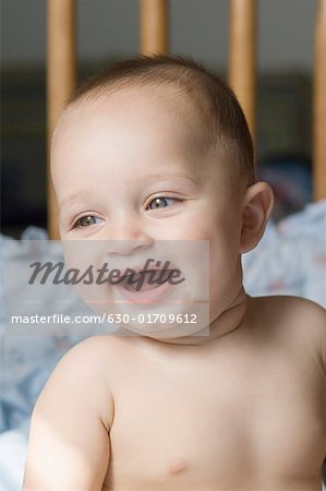 Close-up of a baby boy sitting in a crib and smiling