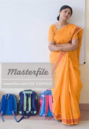 Portrait of a teacher standing beside schoolbags in the classroom