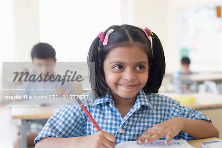 Schoolgirl writing on a notepad in a classroom and smirking