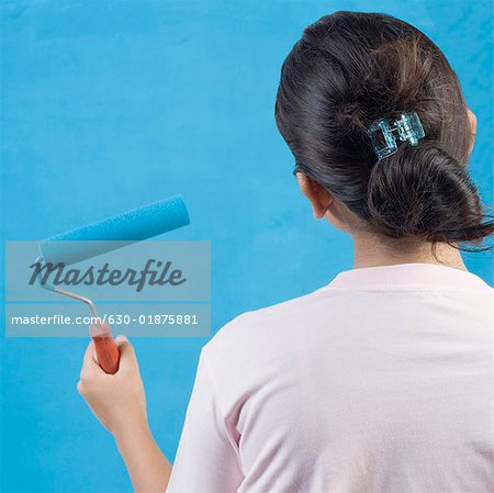 Rear view of a young woman painting a wall with a paint roller